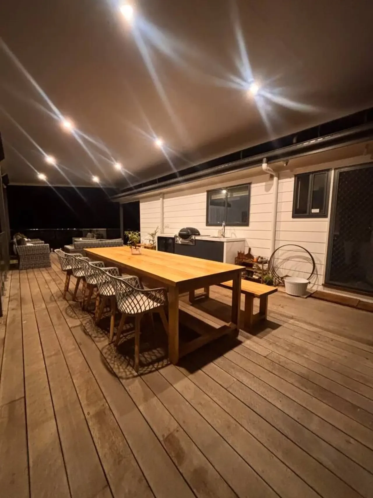 Lancaster Lodge deck at night with dining table and outdoor kitchen lit up