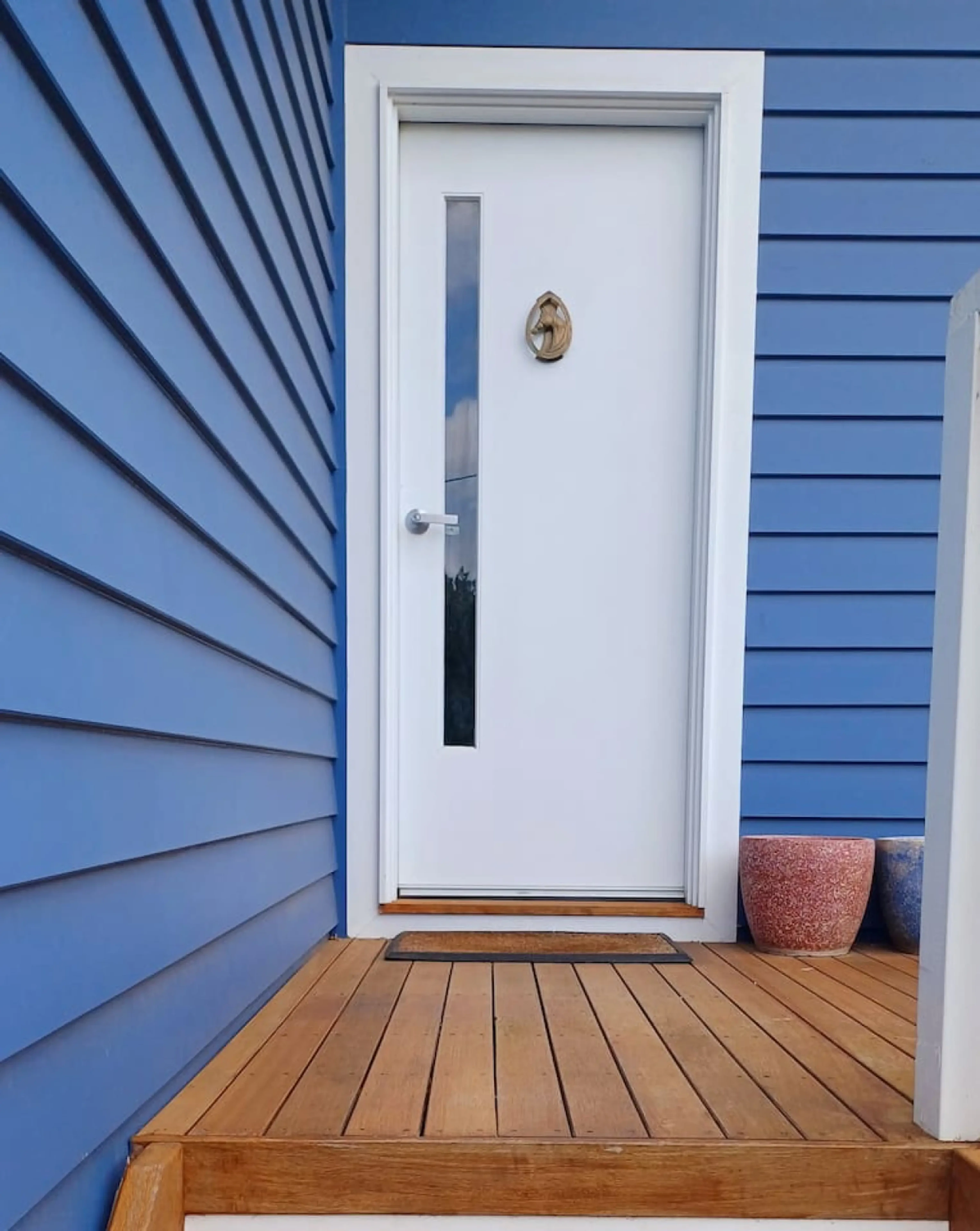 Ocean Blue — white front door with blue cladding and timber decking