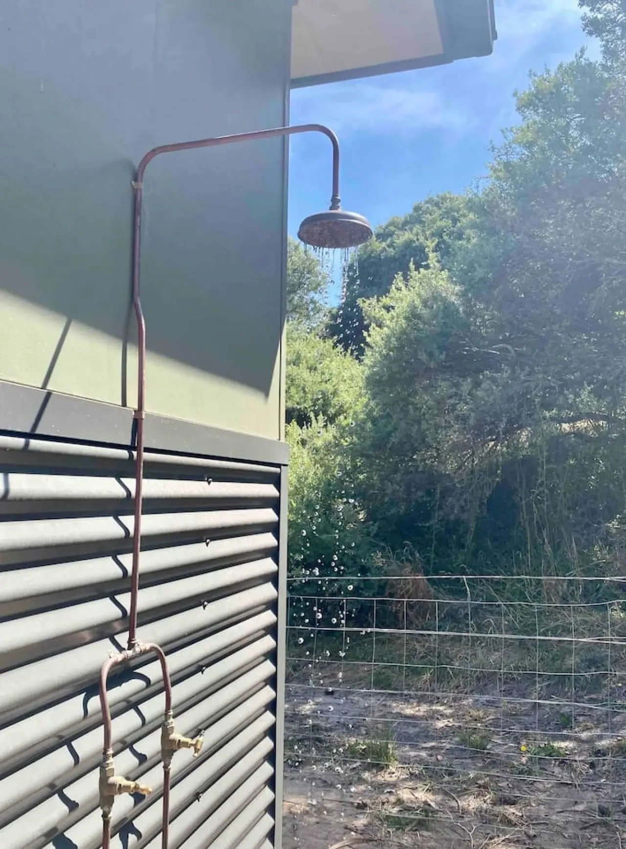 Outdoor shower with copper fittings and bush backdrop